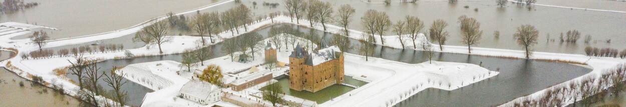 Luchtfoto van Slot Loevestein in een winterlandschap, waarop je ziet dat de toegangswegen naar het kasteel zijn afgesloten vanwege hoogwater