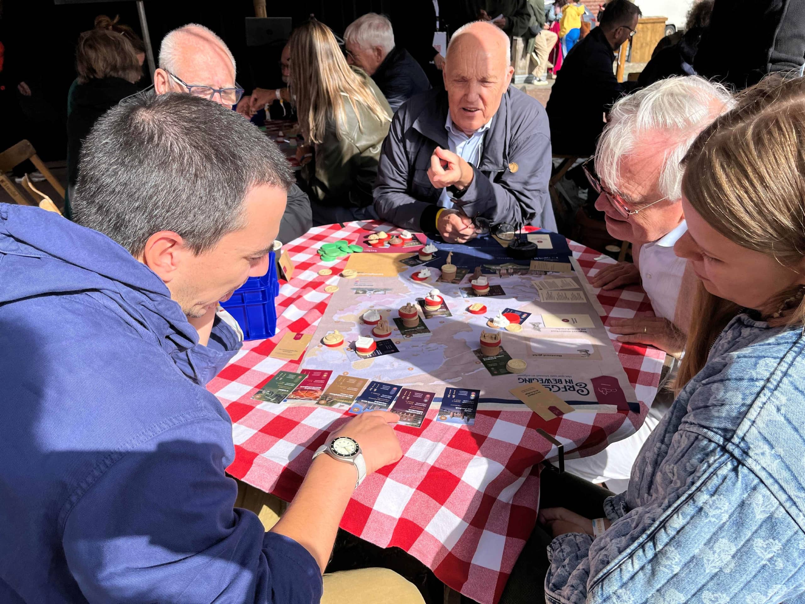 Vijf mensen spelen een bordspel aan een tafel op een terras.