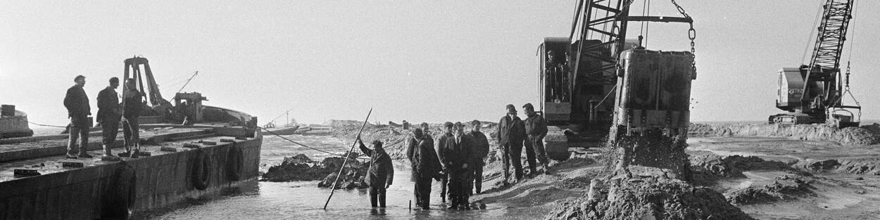 Zwart-wit foto een graafmachine met mannen ernaast.