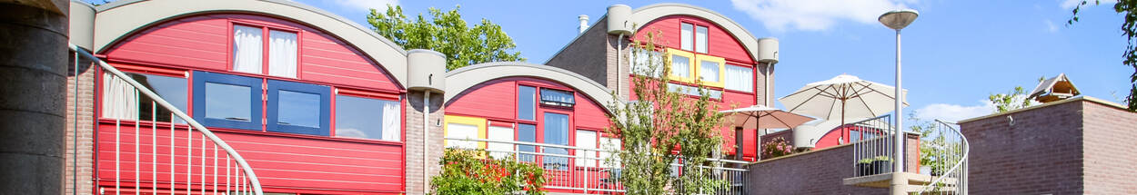 Drie huizen in een hof, rode gevels met gele accenten, ronde vormen, een wenteltrap en dakterras. Genaamd de Wandelmeent in Hilversum.