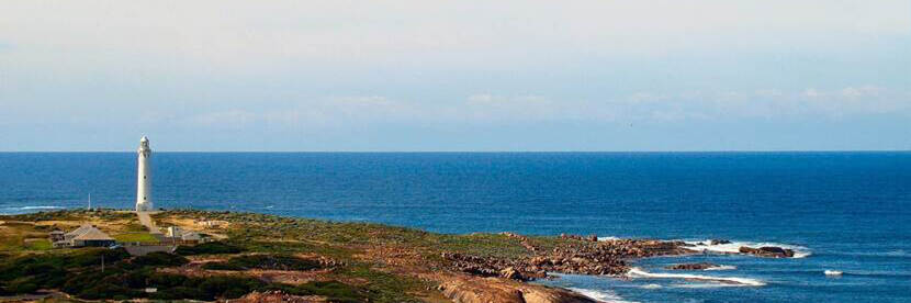 Rotsen langs de kust met een witte vuurtoren en blauwe zee en lucht op de achtergrond