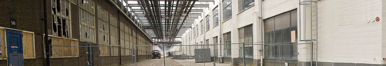 Straat tussen twee vervallen fabrieksgebouwen afgesloten met een bouwhek