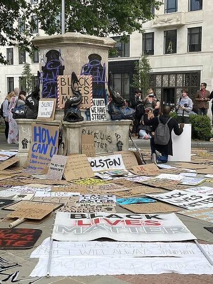 A pedestal with cardboard signs in front and people and a building in the background