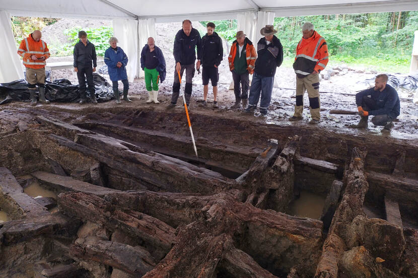 archeologen en vrijwilligers kijken naar opgegraven scheepswrak in de grond