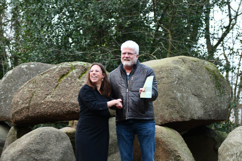 Een particuliere eigenaar (rechts) krijgt een archeologisch rijksmonumentenpaspoort overhandigd van Marjolein Verschuur van de RCE, met in de achtergrond een hunebed D44.