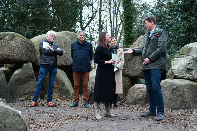 Wout Neutel van Staatsbosbeheer, Marjolein Verschuur van de RCE en de ontvangers van het archeologische rijksmonumentenpaspoort, met in de achtergrond een hunebed