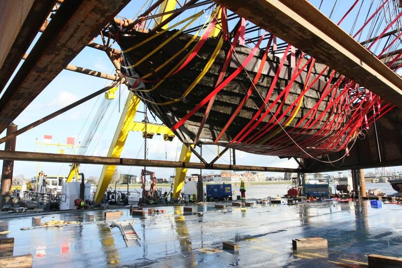 De IJsselkogge, een oud houten schip en archeologische vondst, hangt in banden en is net opgetakeld uit het water.