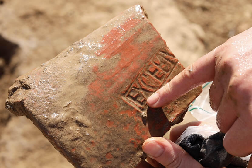 Foto van een dakpan met inscriptie, vastgehouden door een archeoloog