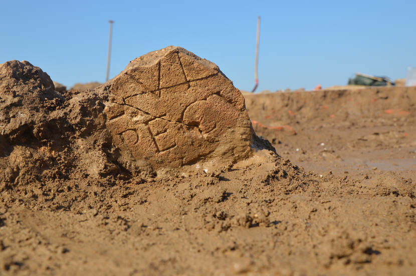 Fragment van een gevonden altaarsteen vanuit een laag standpunt, met schoppen in de achtergrond