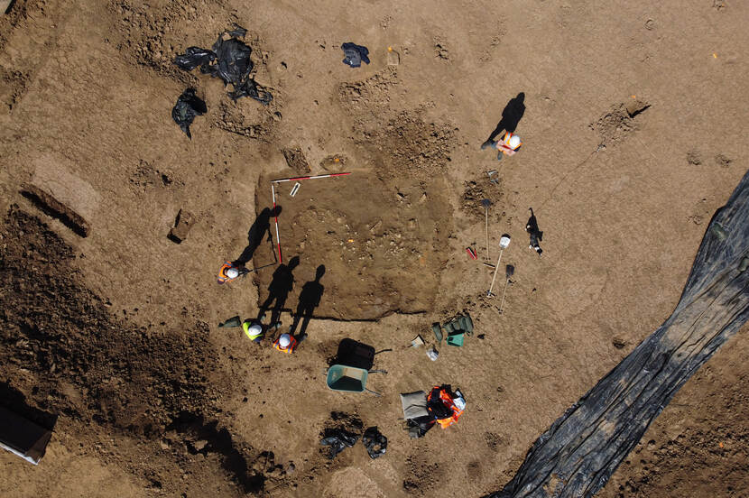 Luchtfoto van de opgraving met medewerkers in oranje hesjes en hun schaduwen
