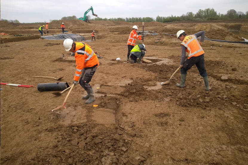 Foto van archeologen die tijdens de opgraving de grond "vlak schaven" met een schop