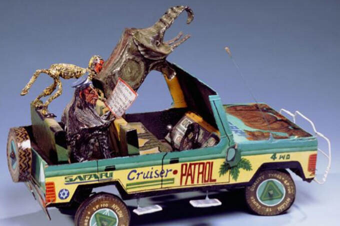 Een miniatuurauto is opgebouwd uit verschillende materialen, zoals karton, ijzerdraad, blik en textiel. In de four-wheel drive zit een olifant, een aap en een chimpansee. Op de motorkap een geschilderde neushoorn. De chimpansee draagt een politiepet en houdt een bord met opschrift in zijn handen. De eerste woorden zijn ‘Now it is our turn’.