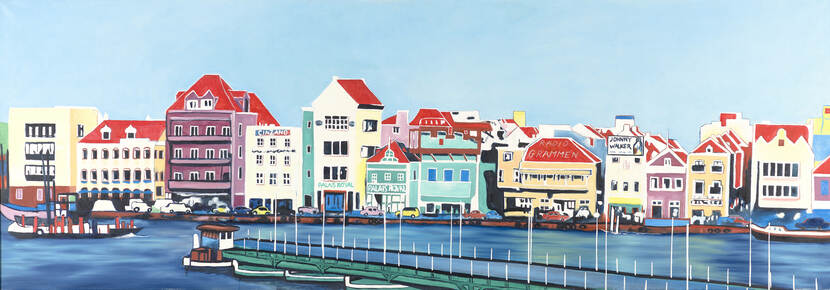 Blik op de huizen aan de Handelskade in Willemstad op Curaçao. Voor de kleurrijke panden ligt de Annabaai; op de voorgrond is de Pontjesbrug te zien.