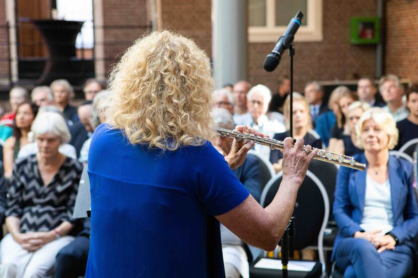 Foto van het achterhoofd van een fluitiste met op de achtergrond een zaal vol publiek