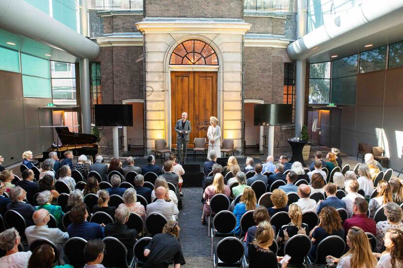 Overzichtfoto van een zaal vol mensen met op het podium twee personen