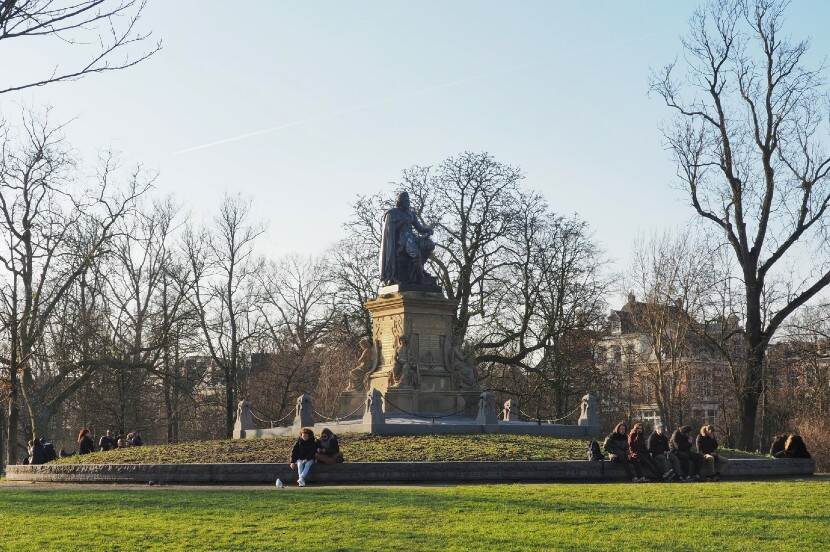 Publiek zittend rond het Vondelmonument, een beeld uit 1867 van brons en Luxemburgse kalkzandsteen, in het Amsterdamse Vondelpark.