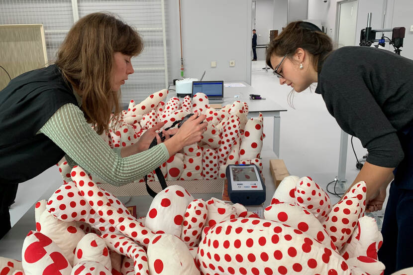 Onderzoekers staan gebogen over een kunstwerk van Yayoi Kusama