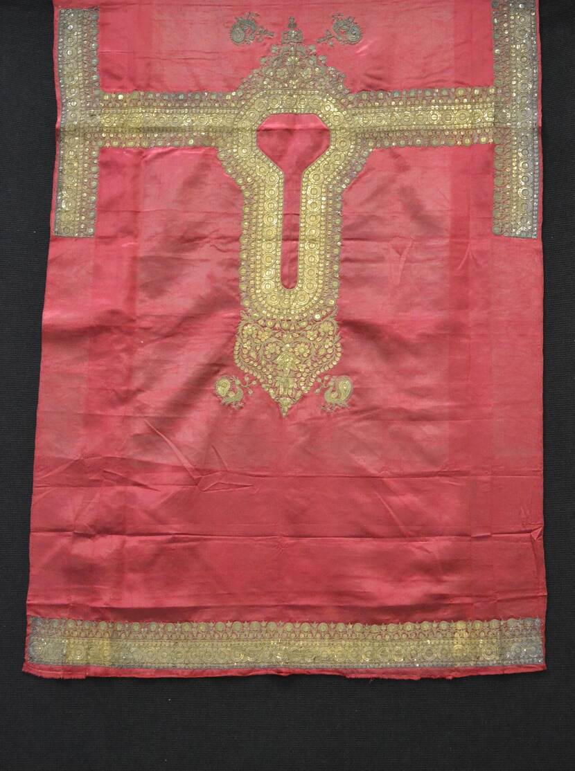 Rode doek met goudborduursel gefotografeerd tegen een zwarte achtergrond.