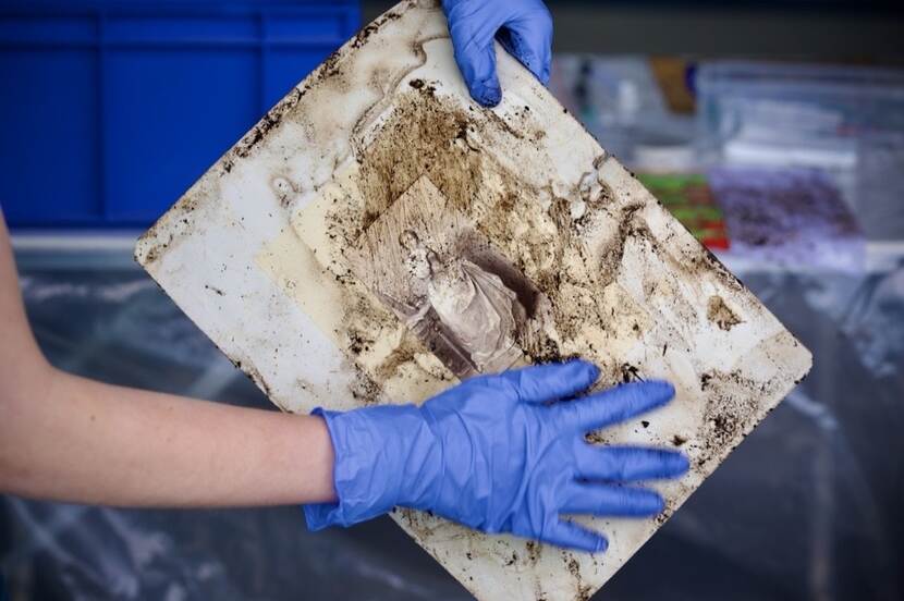 Handen met blauwe handschoenen houden een beschadigd stuk papier vast.