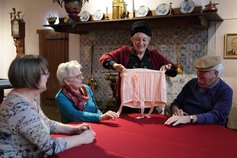 Vrijwilliger toont oude kledij uit reminiscentiekoffer