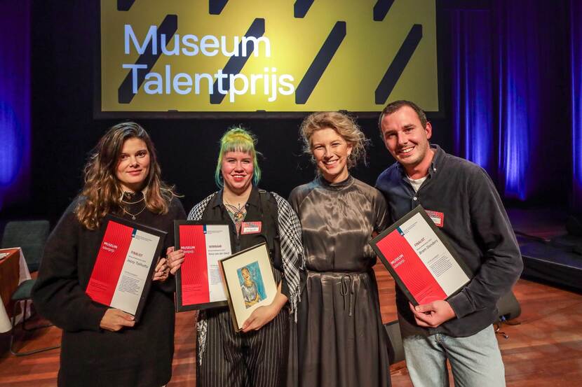 VIer mensen op een podium, waarvan drie met een oorkonde in hun hand