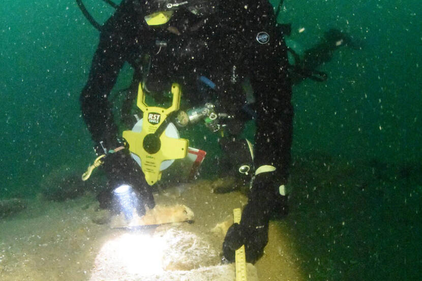 Een archeoloog in duikpak verricht onderzoek op een scheepswrak