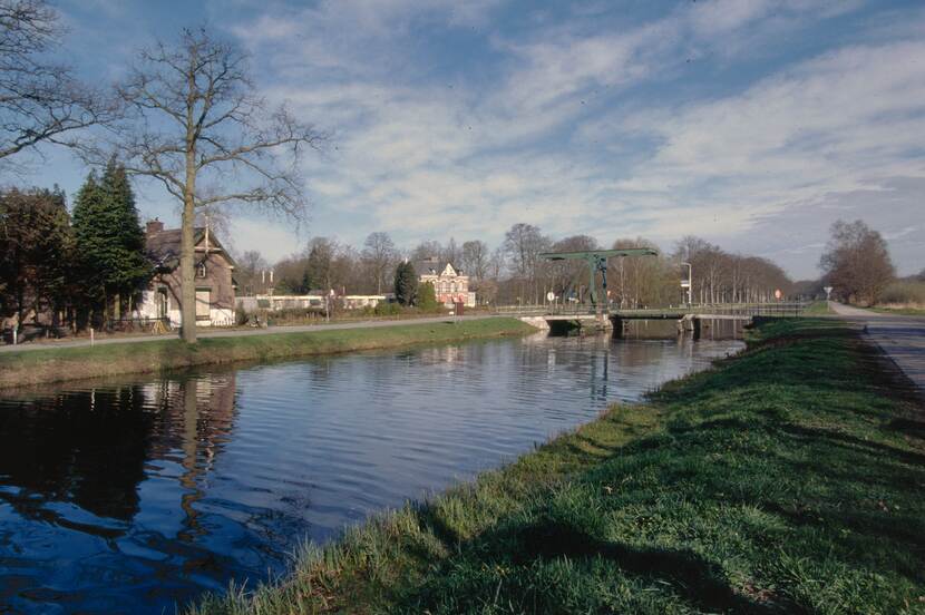 Zicht op een kanaal met aan weerszijden een strook gras en in de verte een groene ophaalbrug.