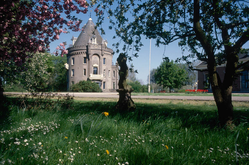 Zicht op een ronde toren met spits dak. Op de de voorgrond bomen met roze bloesem.