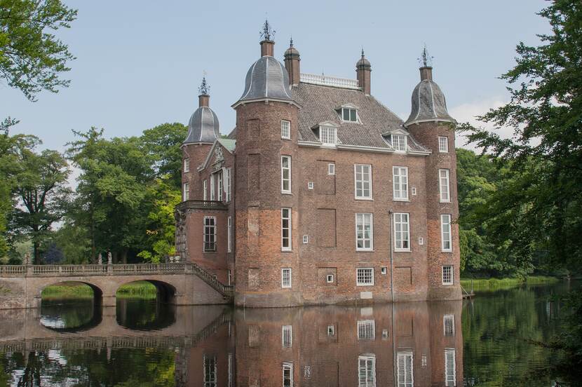 Zicht op een vierkant kasteel met vier ronde hoektorens, omringd door een gracht.