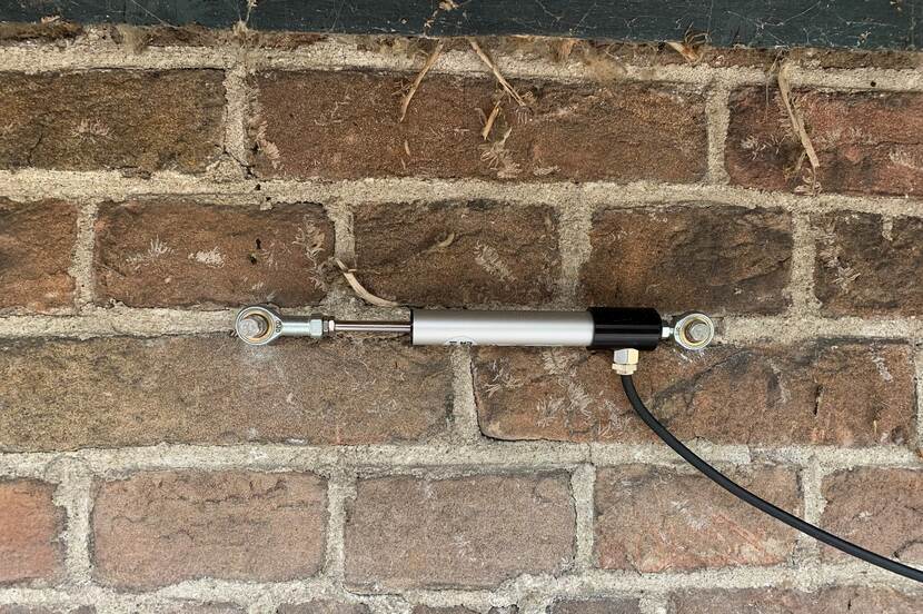 Foto van de datalogger, het instrument dat de scheuren in het gebouw meet. Een horizontaal bevestigde buis is te zien, met daarachter de bakstenen van het gebouw.