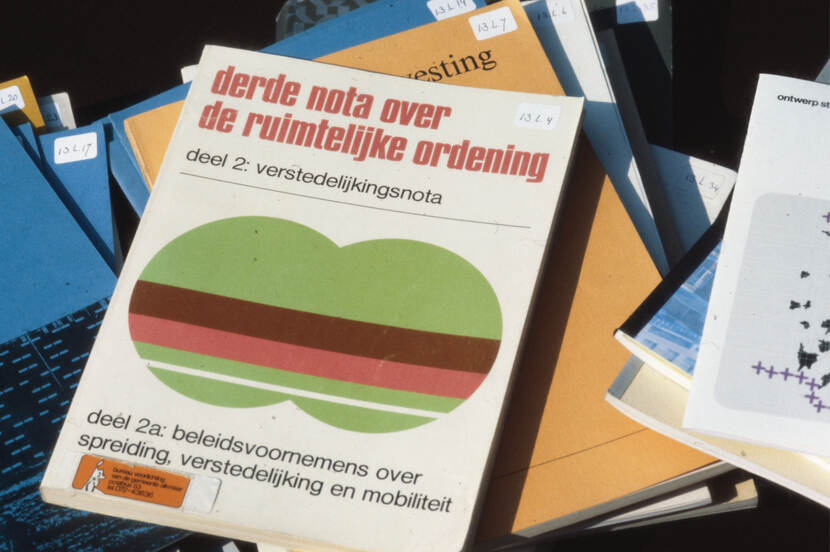 Stapel boeken met in het midden de derde nota. Op de kaft van het boek staat: derde nota over de ruimtelijke ordening, deel 2: verstedelijkingsnota, deel 2a: beleidsvoornemens over spreiding, verstedelijking en mobiliteit