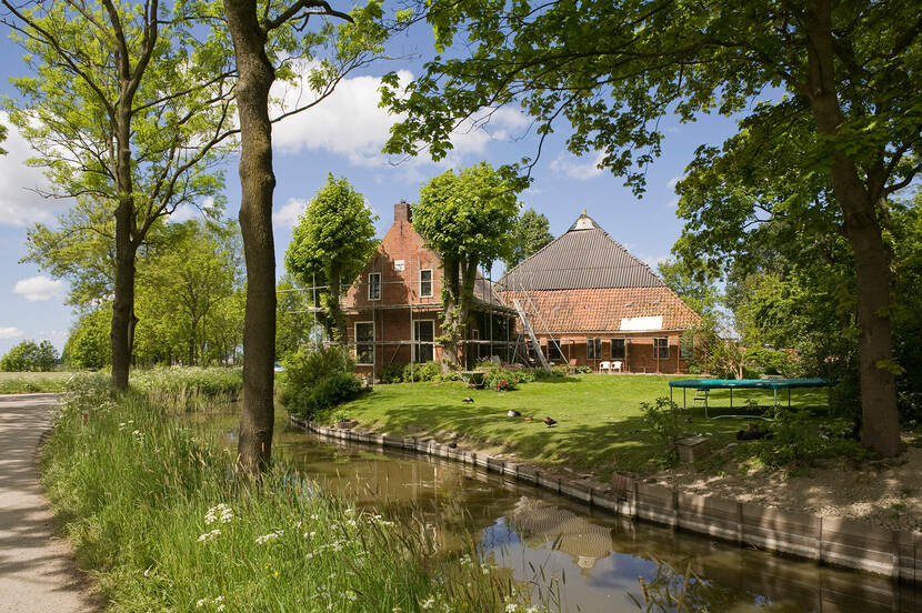 Boerderij in de steigers met grasveld en trampoline en bloeiend fluitekruid langs de sloot