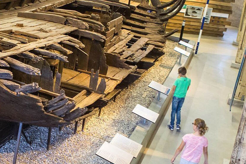 Resten van een schip in het museum Batavialand in Lelystad, met twee kinderen die er omheen lopen.