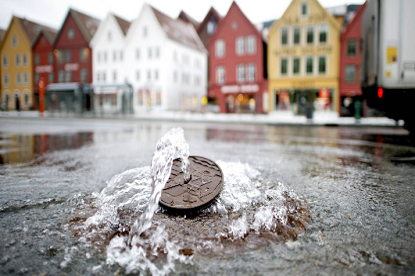 Water komt omhoog uit de put met huizen in de haven van Bryggen in Noorwegen op de achtergrond