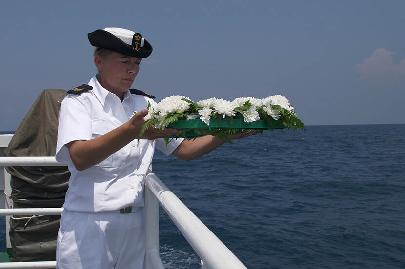 Vrouwelijke marinier staat op het punt om vanaf een schip een blad met witte bloemen in zee te gooien
