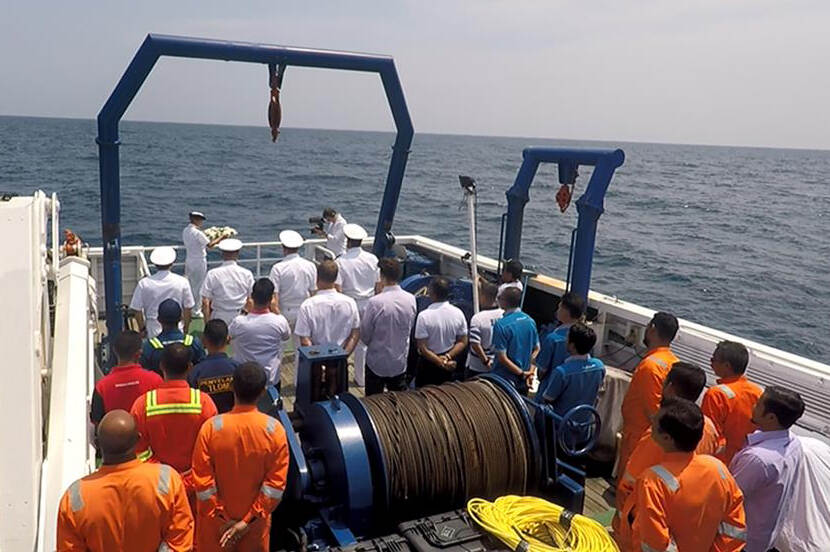 Een groep mensen aan boord van een schip op zee tijdens een herdenkingsbijeenkomst