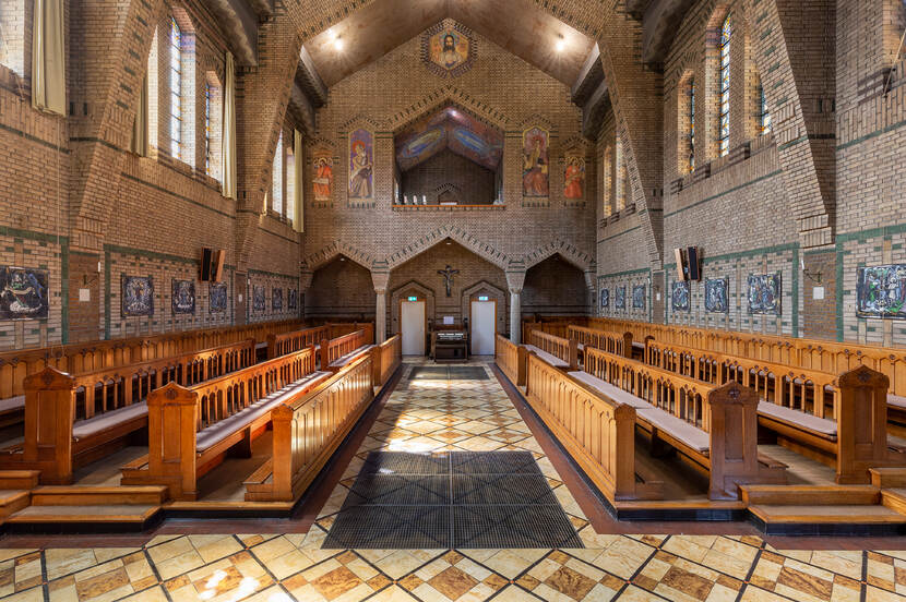 Zicht richting het altaar van de gebedsruimte in een kloosterkapel, met aan weerszijden houten kerkbanken.