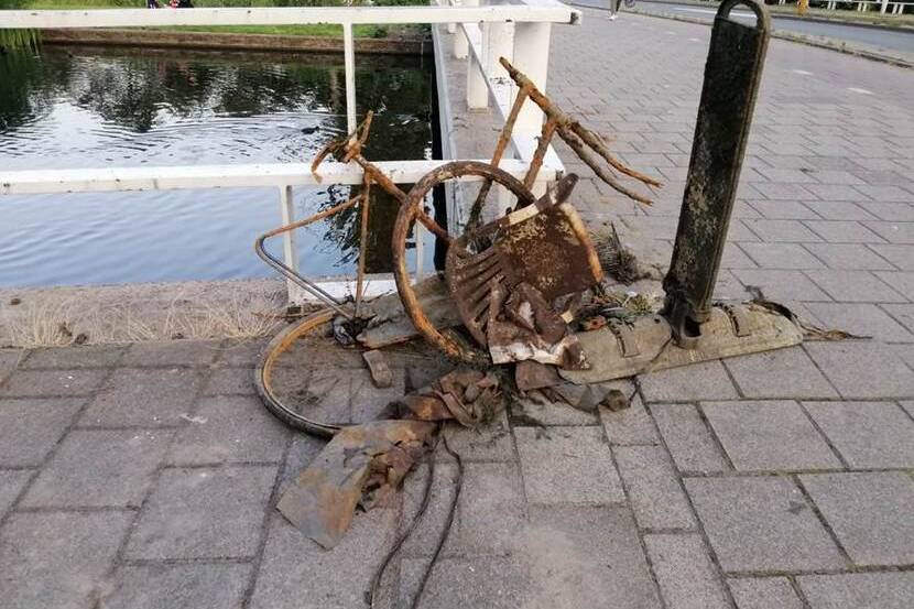 Roestige metaalonderdelen, waaronder een fietswiel, uit een gracht gevist en achtergelaten op de stoep
