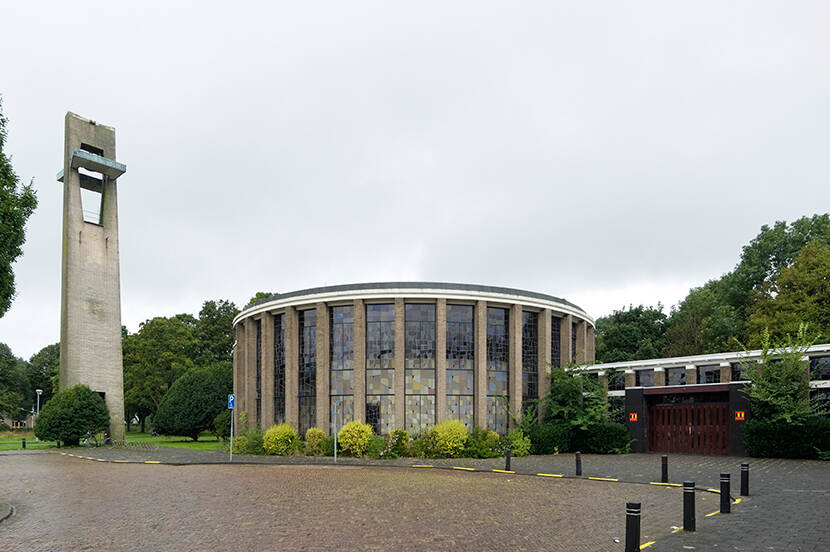 Exterieur van de Sint-Jozef Opifexkerk met in het midden de ronde glas-in-loodgevel en links de klokkentoren