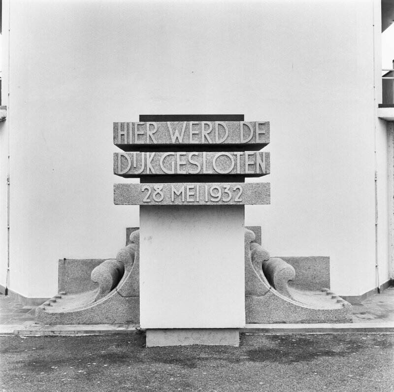 Zwart-wit foto van een monument op de afsluitdijk, waarop staat: Hier werd de dijk gesloten, 23 mei 1932