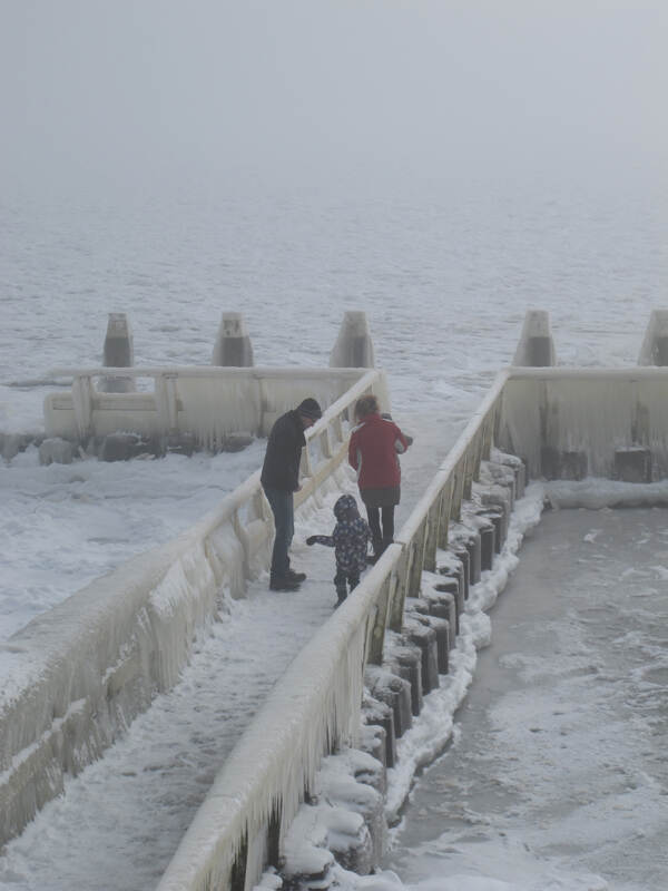 Een vader, moeder en kind lopen in de sneeuw bij de afsluitdijk