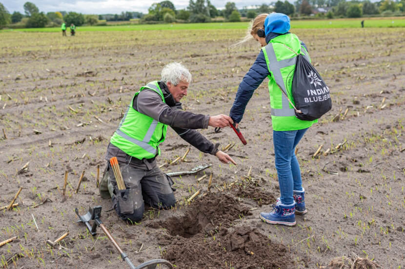 Foto van een archeoloog in het veld met een scholier die hem helpt
