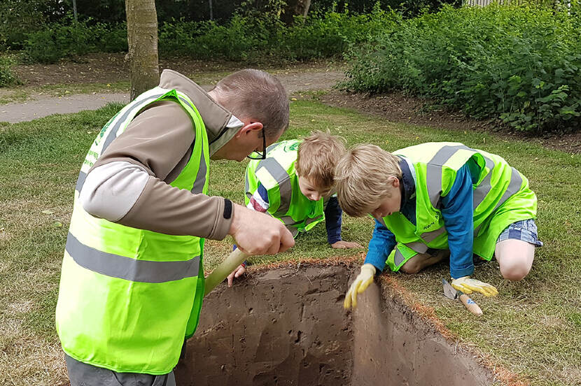 Foto van een archeoloog en twee kinderen bij een diepe kuil