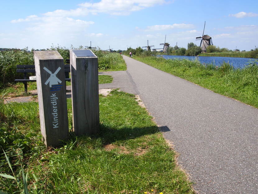 Smalle weg langs paaltjes waarop 'Kinderdijk' staat. Op de achtergrond staan molens.