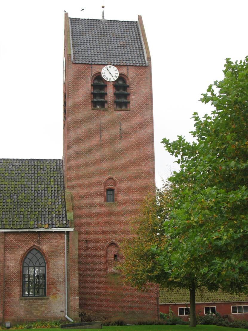 Rode bakstenen kerktoren met een boom ernaast.