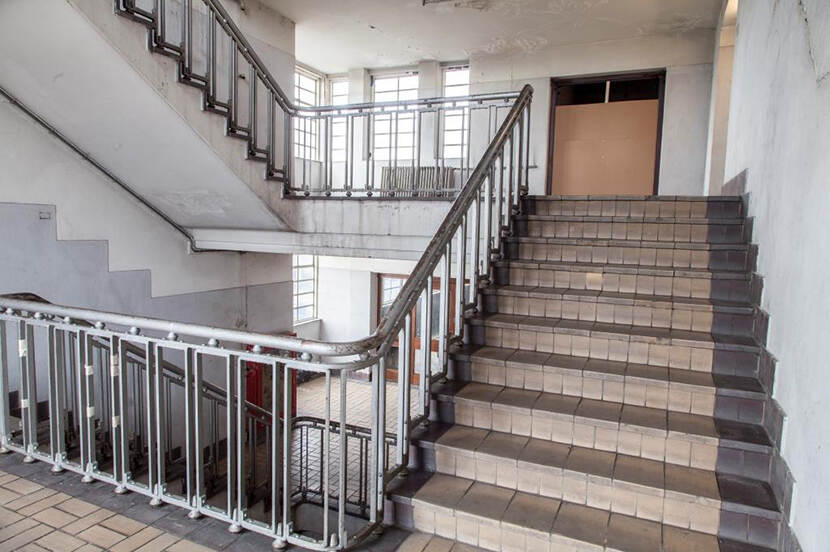 Het betegelde trappenhuis met buisleuning en gele vloerklinkers in metselmozaïek