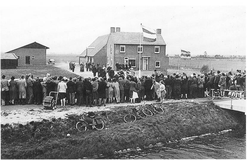 Mensen staan in een groep te kijken naast een huis waar een vlag wappert