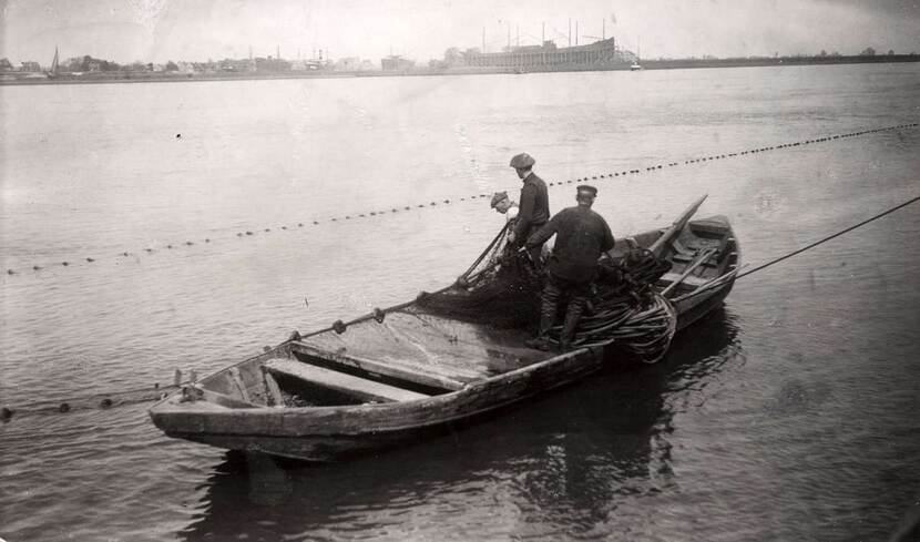 Een zwart-wit foto van drie vissers in een houten bootje.