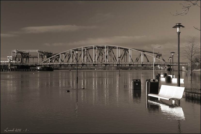 Zwart-wit foto van de overstroomde kade van de IJssel.