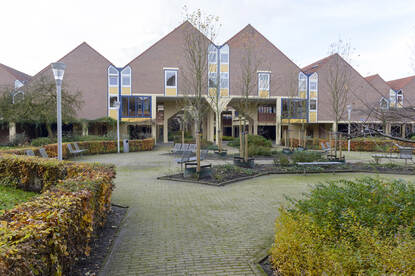 Een rij woningen met puntdaken met op de voorgrond een plein met bankjes.